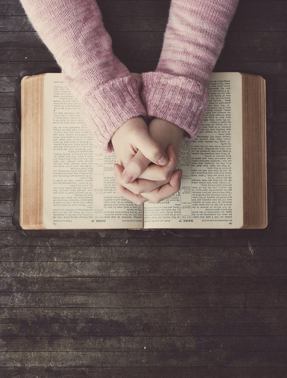 Hands clasped together over an open book on a wooden surface, illustrating "Who We Are".