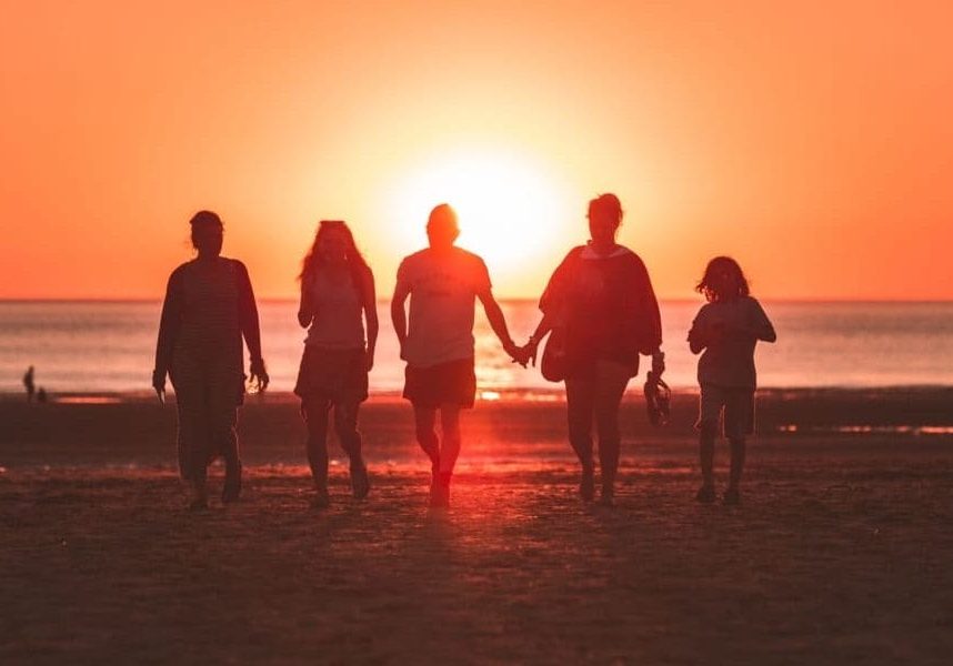 A group of individuals holding hands and walking on the beach at sunset to pray for friends.