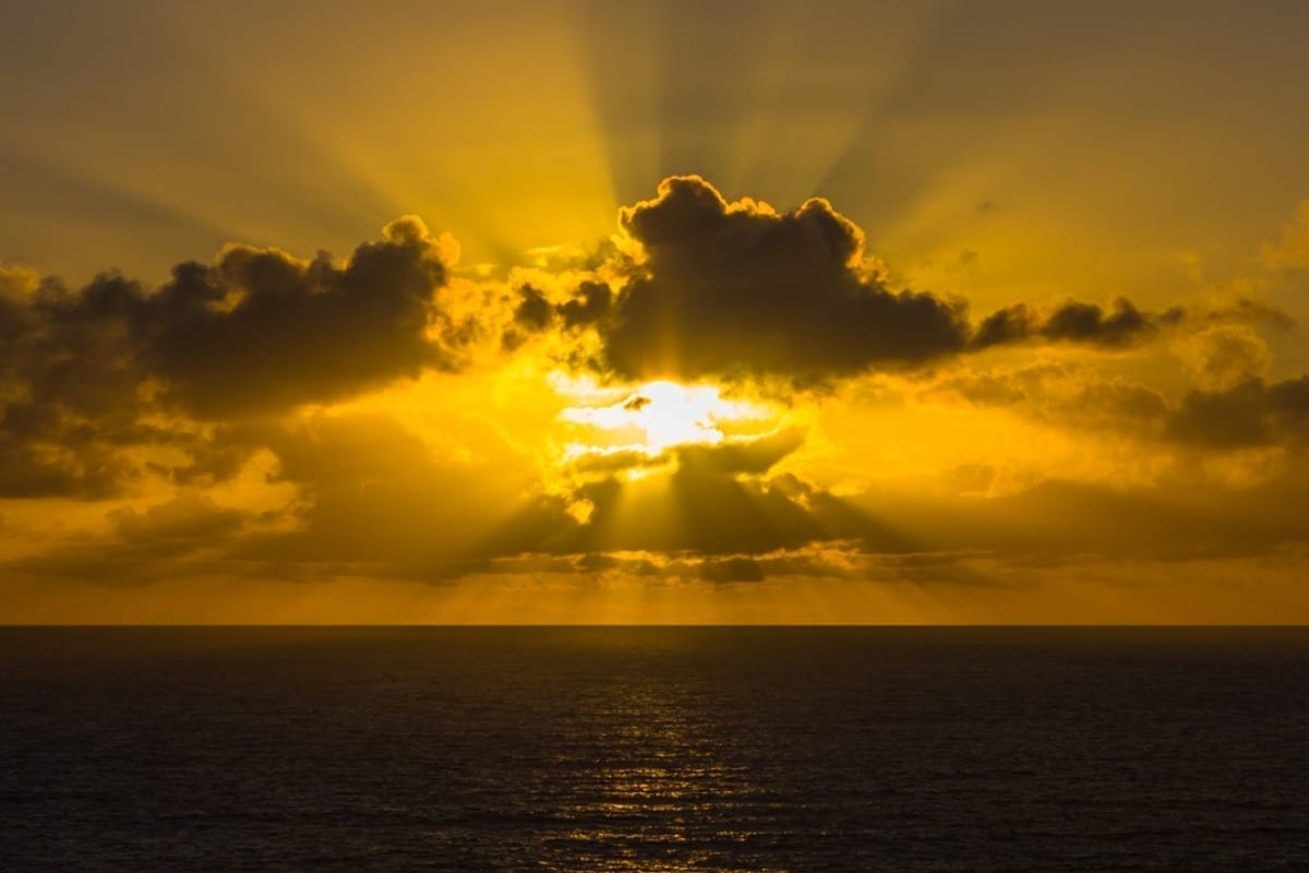 Sunset over the ocean with rays of sunlight breaking through the clouds.