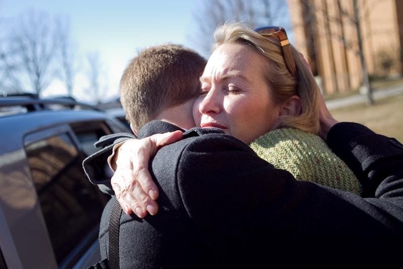 Two people embracing each other in an emotional hug outdoors, praying for their children moving away from home.